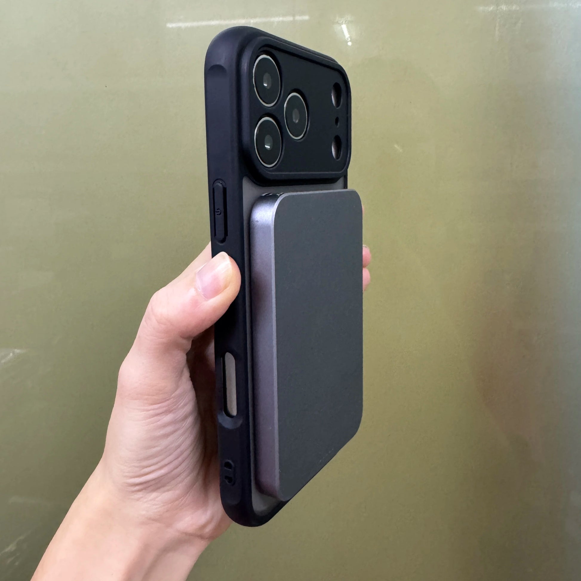 Hand holding a black Iphone 17 Pro/ Pro max in a Matte black case being charged with a Magsafe wireless power bank